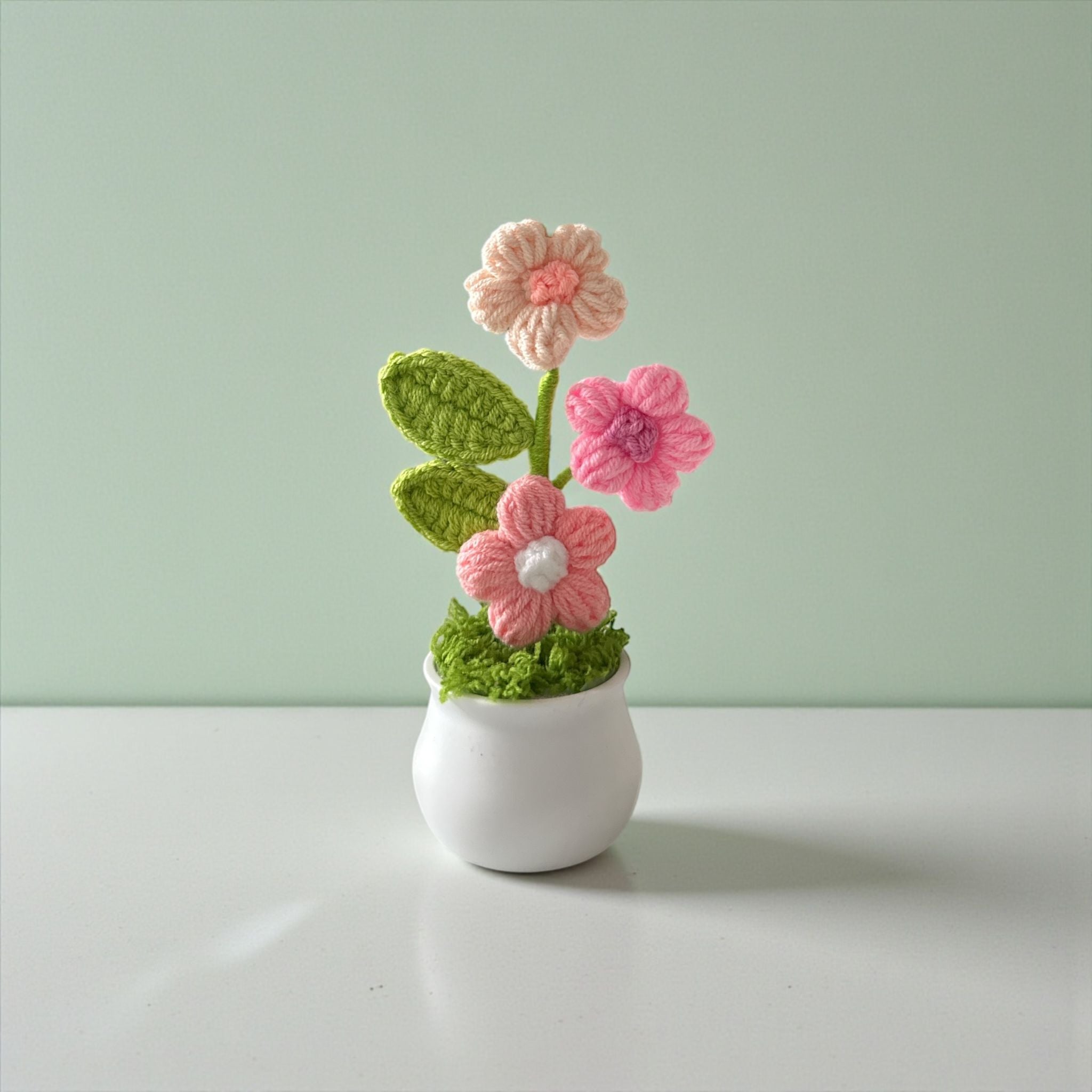 Crocheted pink flowers in a white pot on a light green background