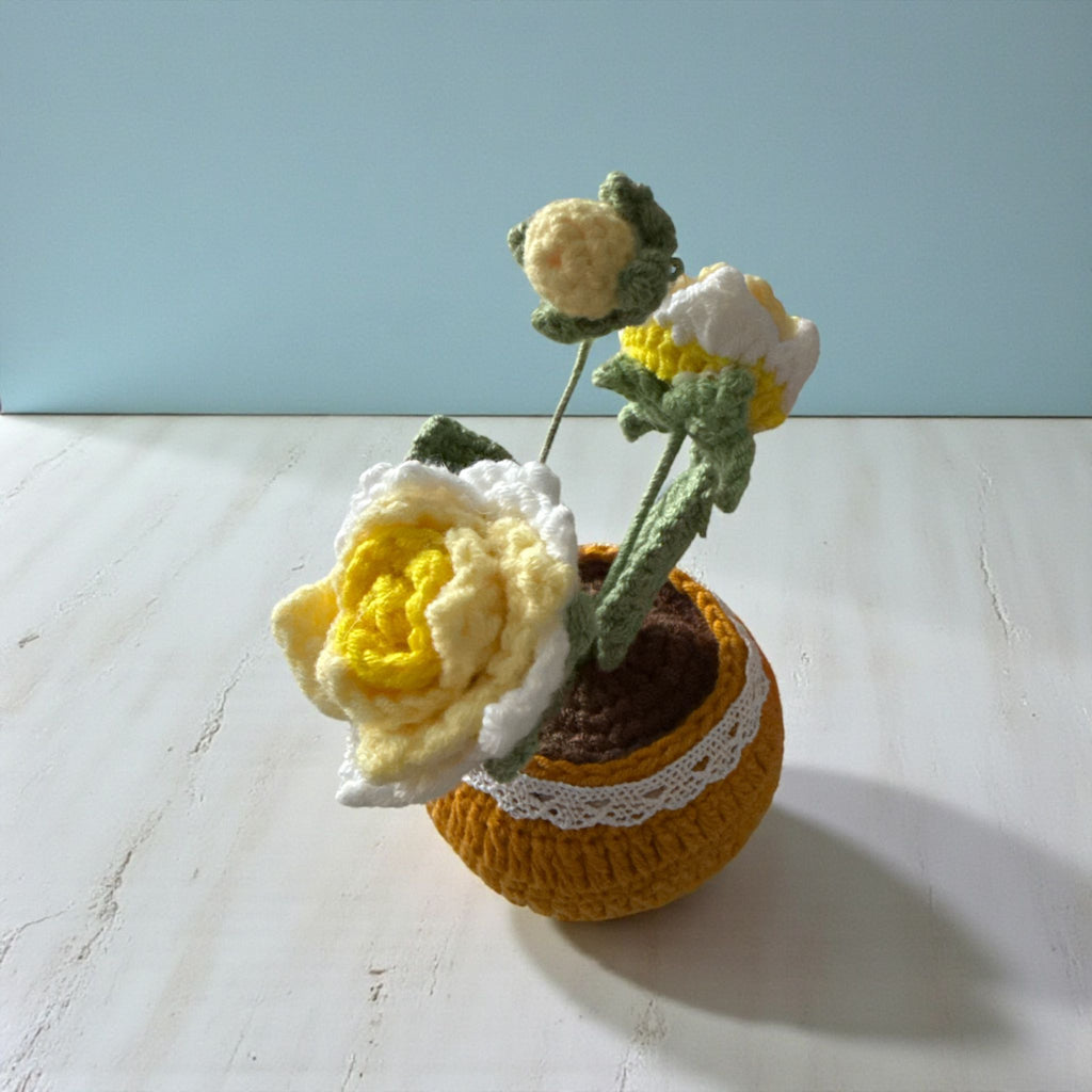 Knitted flower arrangement in a pot on a light surface with a blue background
