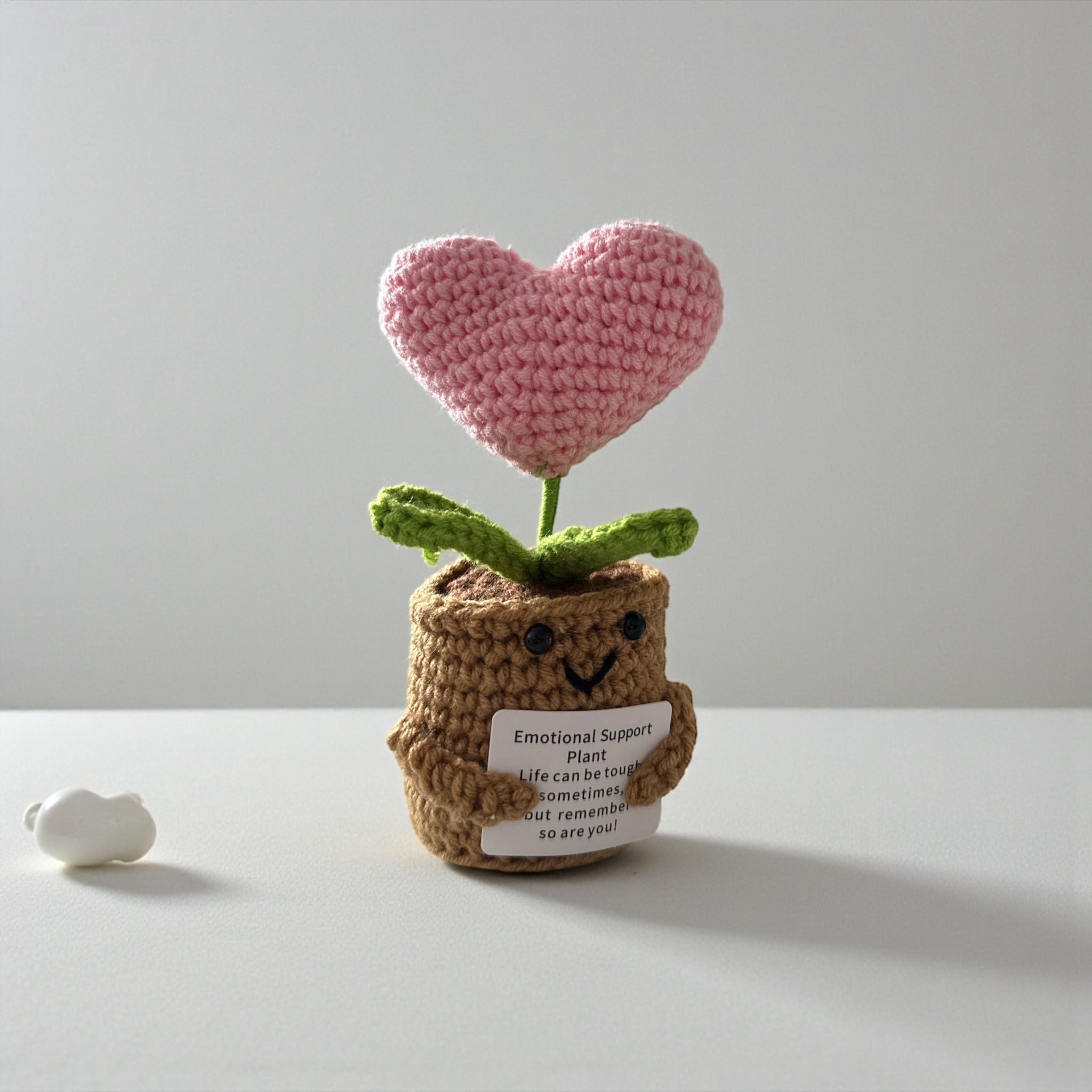 Crocheted heart plant in a brown pot with a message tag on a light gray background