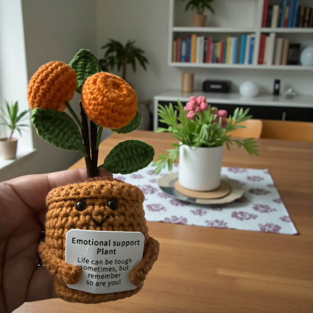 Hand holding a crocheted emotional support plant with a message in a home setting.