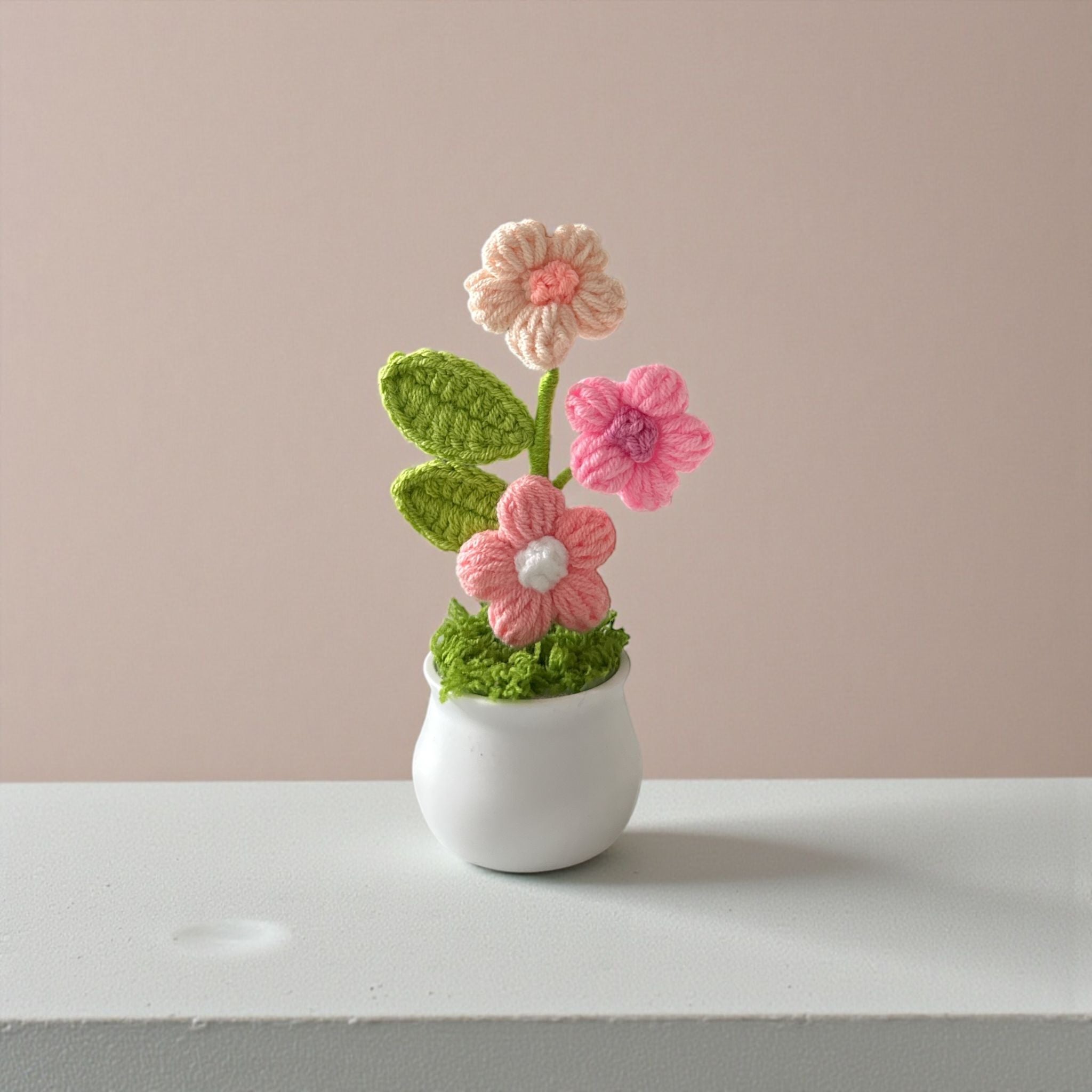 Crocheted flower arrangement in a small white pot on a plain background