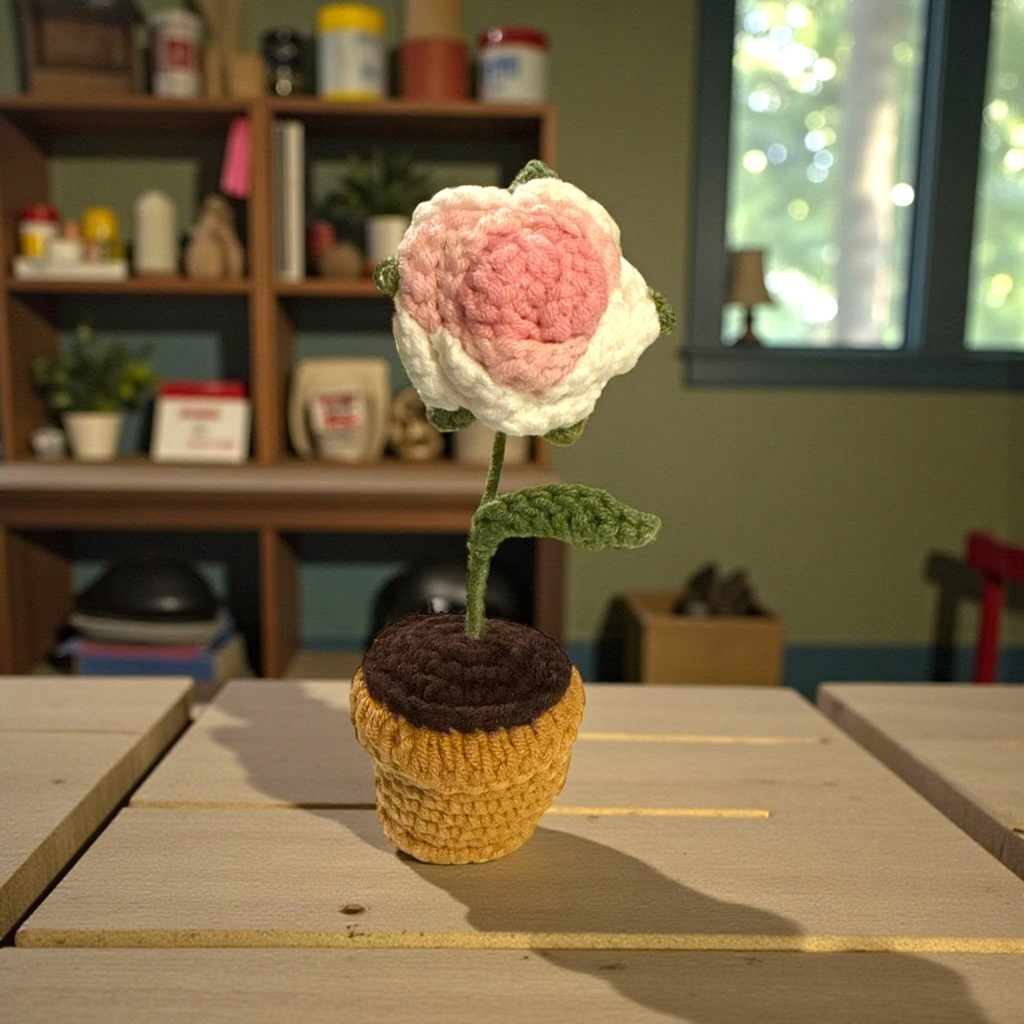 Crocheted flower in a pot on a wooden surface with a blurred background