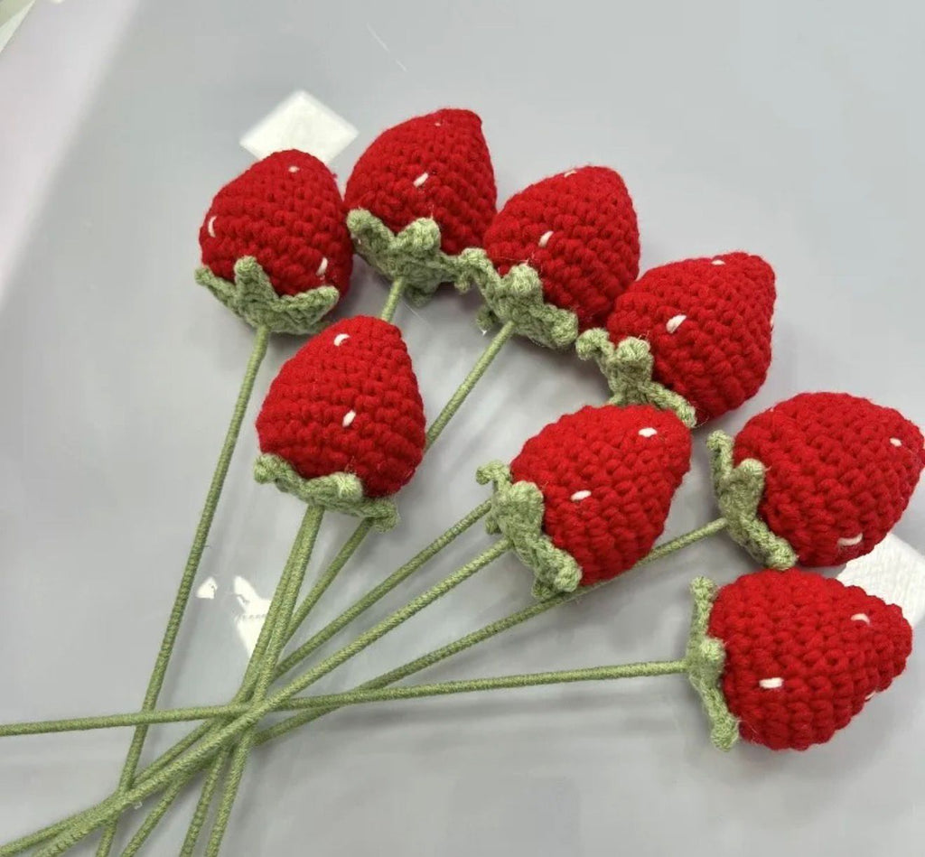 Crocheted red strawberries with green stems on a white background