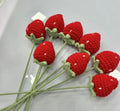 Crocheted red strawberries with green stems on a white background