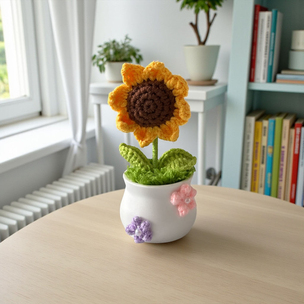 Knitted sunflower in a white pot on a wooden table with a cozy room background.