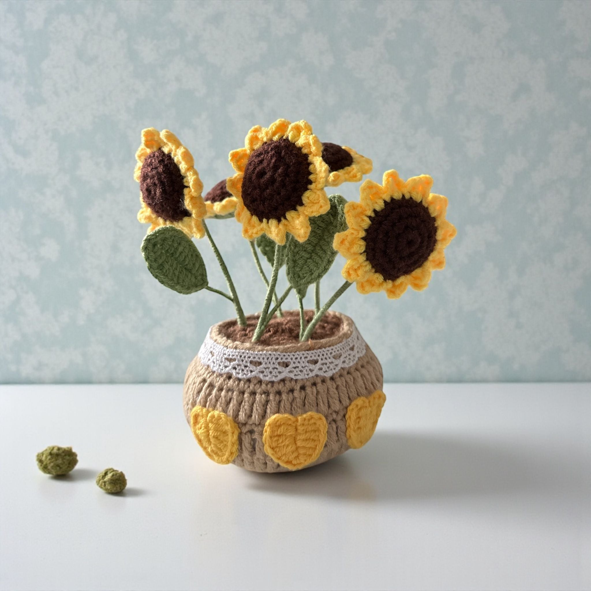 Crocheted sunflowers in a pot on a light surface with a light blue textured background