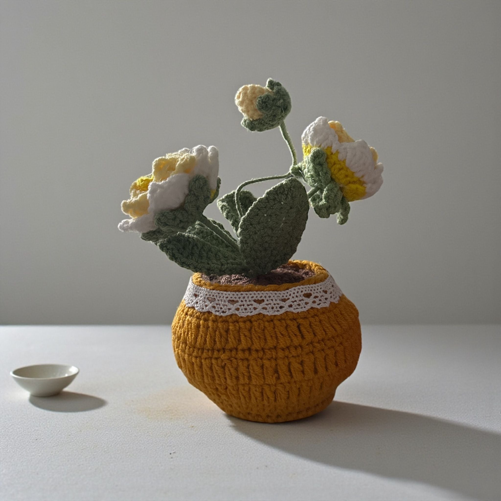 Knitted potted plant with flowers on a plain background