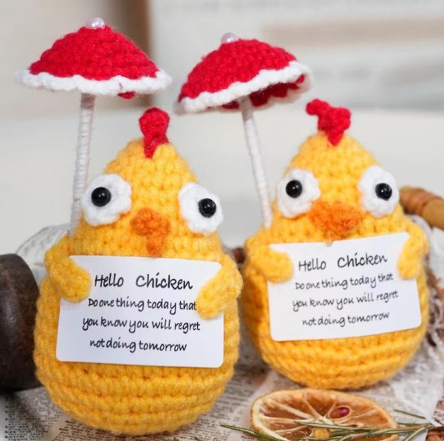 Two crochet chickens with red hats and motivational cards on a textured surface.