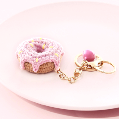 Pink donut-shaped keychain with a gold chain on a pink background