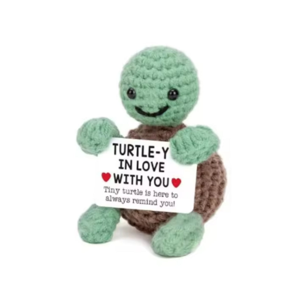 Crocheted turtle toy holding a sign saying 'Turtle-y in love with you' on a white background