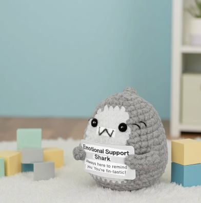 Plush toy shark with a sign labeled 'Emotional Support Shark' on a carpeted floor with colorful blocks.