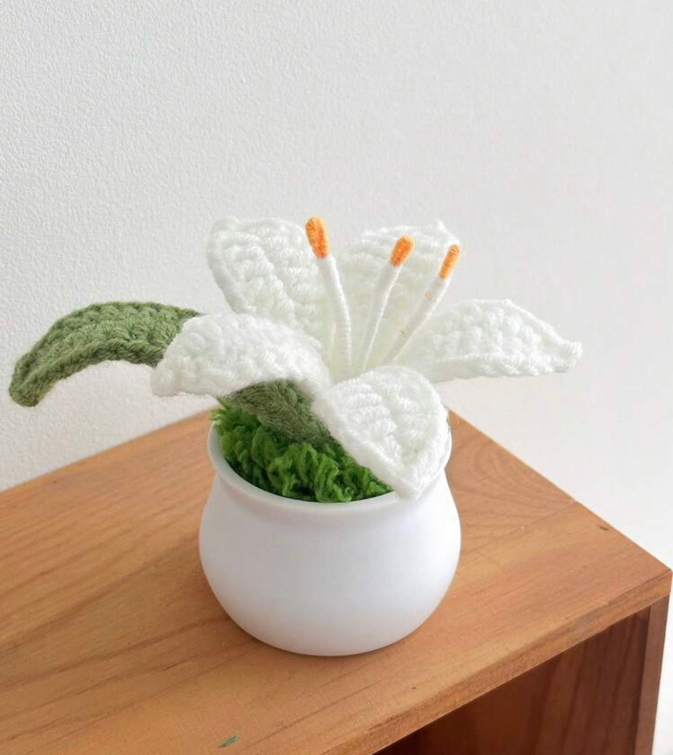 Decorative white flower with green leaves in a white pot on a wooden surface.