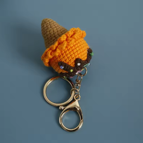 Crocheted character keychain with a brown hat and orange body on a blue background