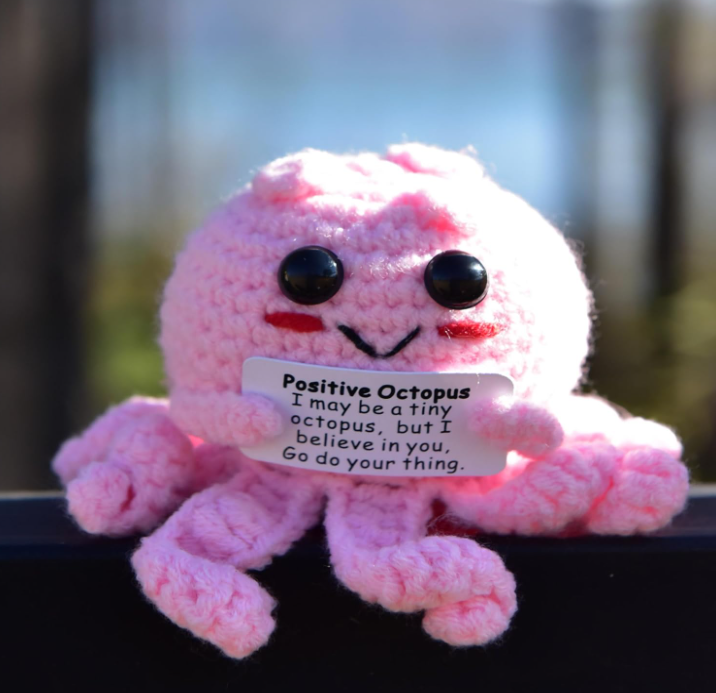 Pink plush octopus with a motivational message tag against a blurred natural background