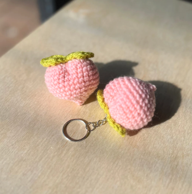 Pink crochet peach keychain with yellow stem on a light surface