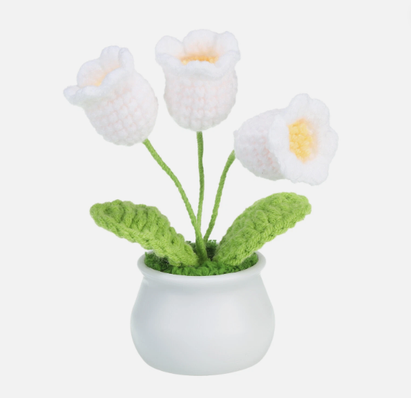 Knitted white flowers with green leaves in a white pot on a white background