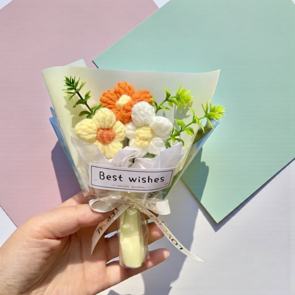 Hand holding a small bouquet of crocheted flowers with a 'Best wishes' card on a colorful background.