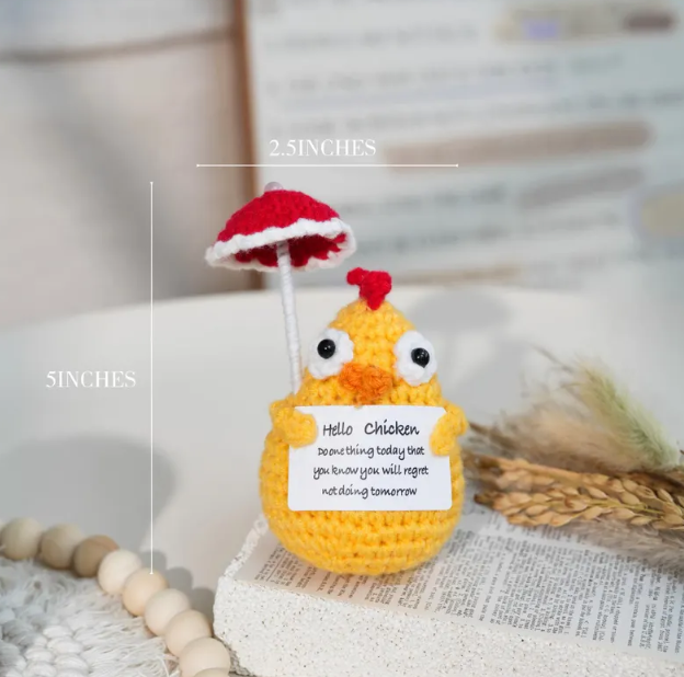 Crocheted yellow chicken with a red umbrella and humorous message on a neutral background