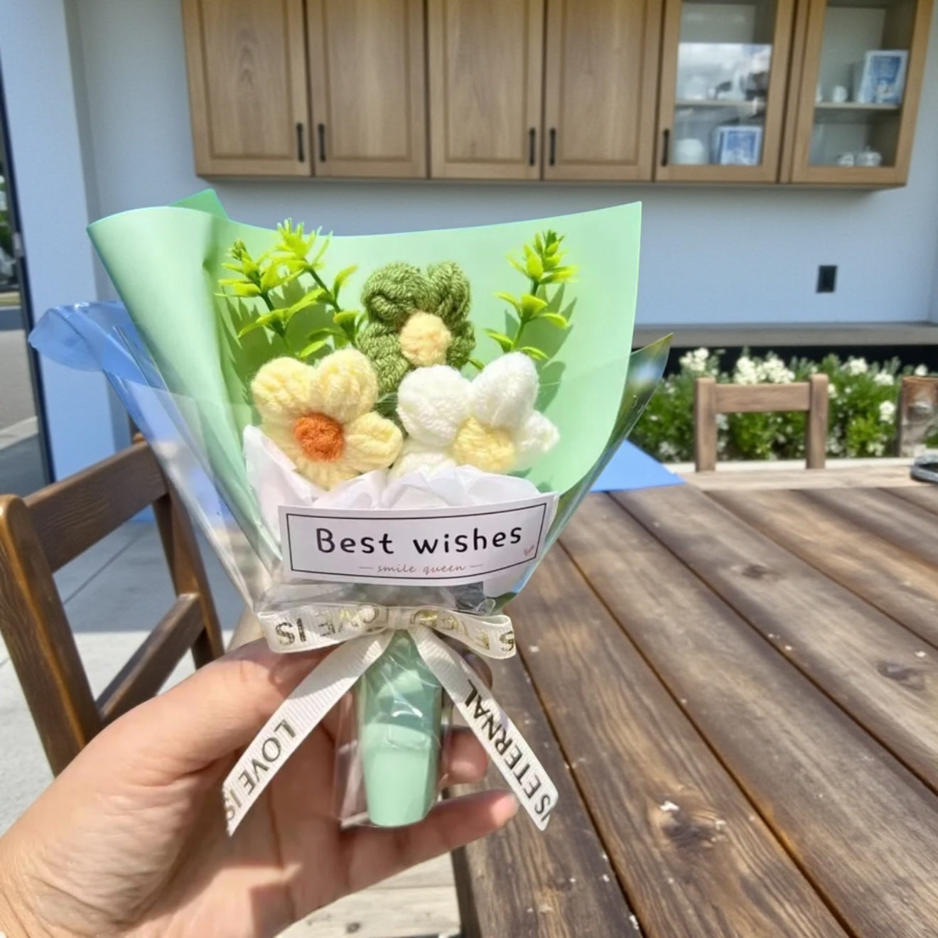 Bouquet of soap flowers with 'Best wishes' card held by a hand outdoors.