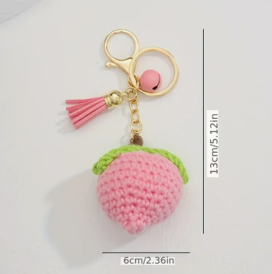 Pink crocheted fruit-shaped keychain with a gold clasp and pink tassel on a white background.