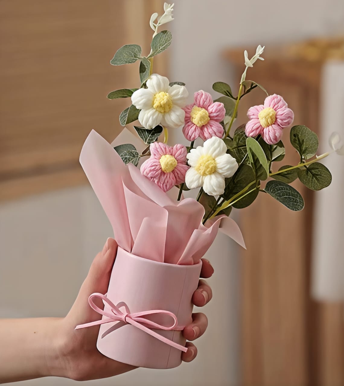 Bouquet of flowers wrapped in pink paper held by a hand against a neutral background