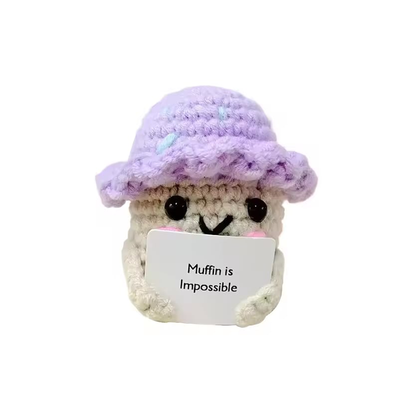 Crocheted character with a purple hat and a sign saying 'Muffin is Impossible' on a white background