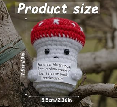 Crocheted mushroom toy with a red cap and white body, sitting on a branch with measurement text overlay.