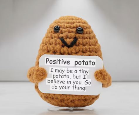 Crocheted potato with a sign saying 'Positive potato' on a plain background