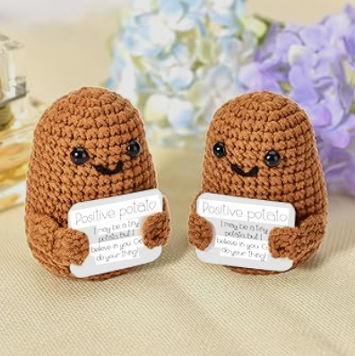 Two brown crochet toys with a message card on a beige surface with flowers in the background
