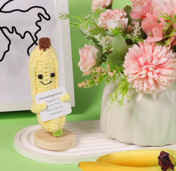 Plush banana toy with a smiling face next to a vase of pink flowers on a green background