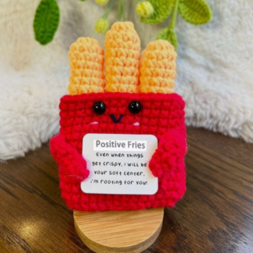 Crocheted fries with a red bun and a message tag on a wooden surface.
