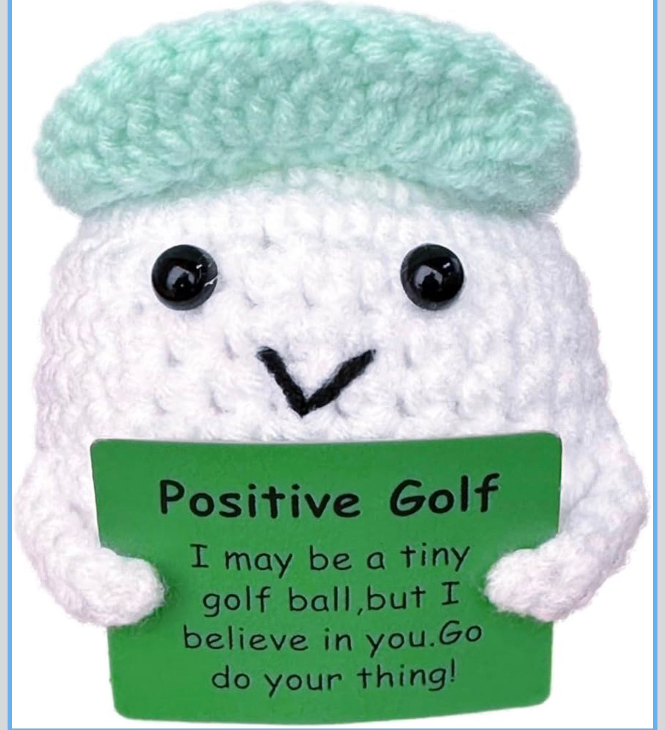 Crocheted golf ball character with a green hat and sign reading 'Positive Golf' on a blue background.