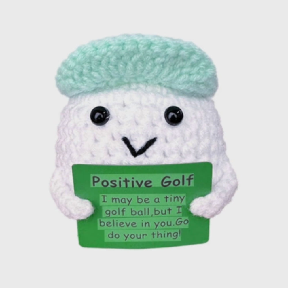 Crocheted golf ball character with a green sign and light blue cap on a white background