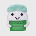 Crocheted golf ball character with a green sign and light blue cap on a white background