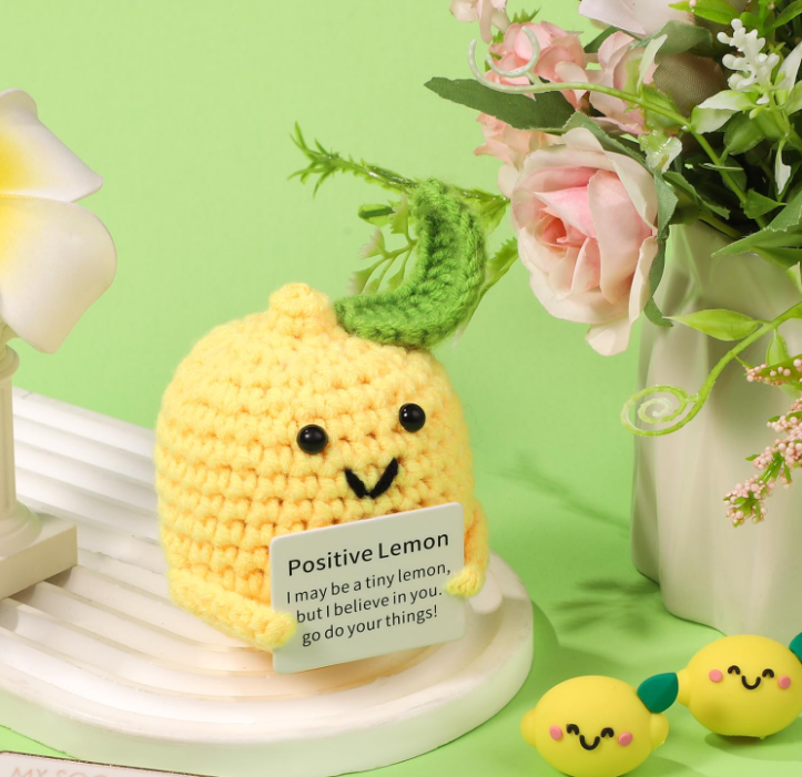 Crocheted lemon character with a motivational message on a green background with flowers.