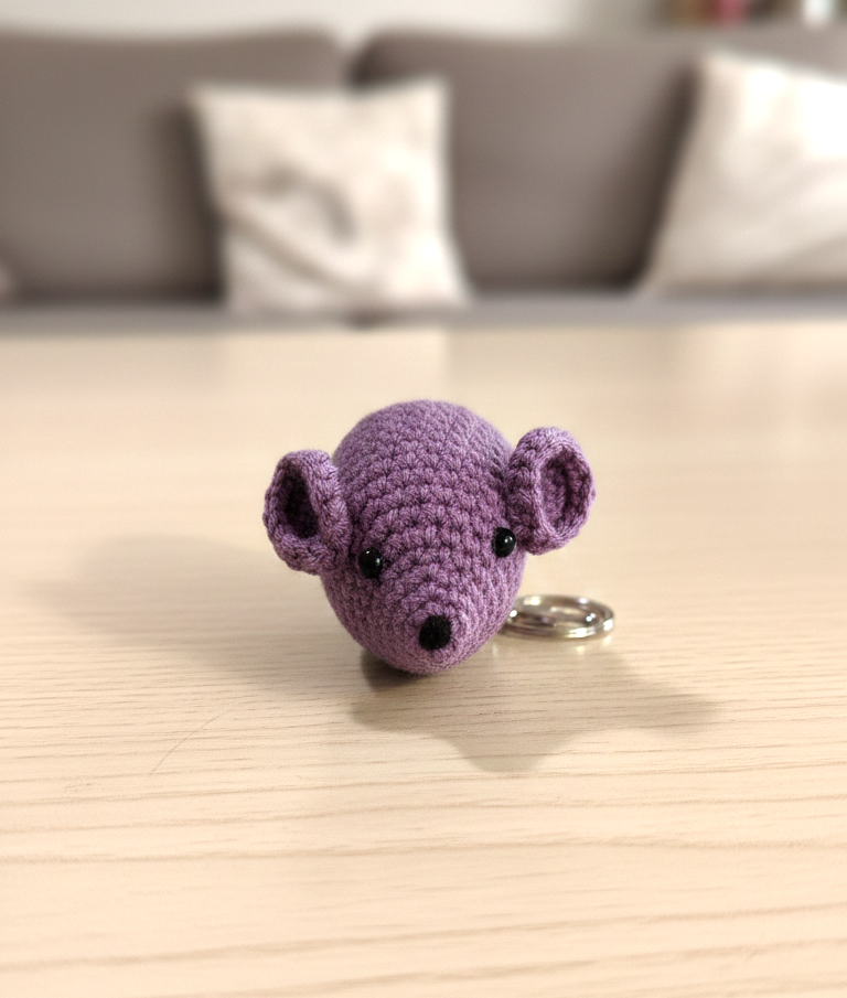 Purple crochet mouse keychain on a wooden surface with a blurred background