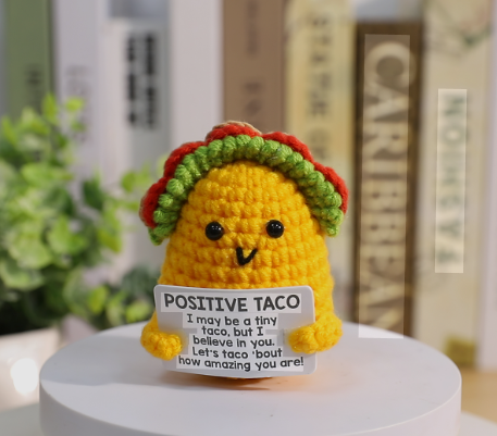Crocheted Positive Taco toy with a sign on a white surface