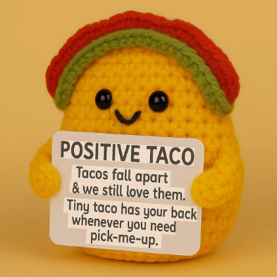 Crocheted taco plushie with a sign on a yellow background