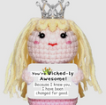 Crocheted doll with blonde hair, pink dress, and tiara holding a sign saying 'You're Wicked-ly Awesome!'.