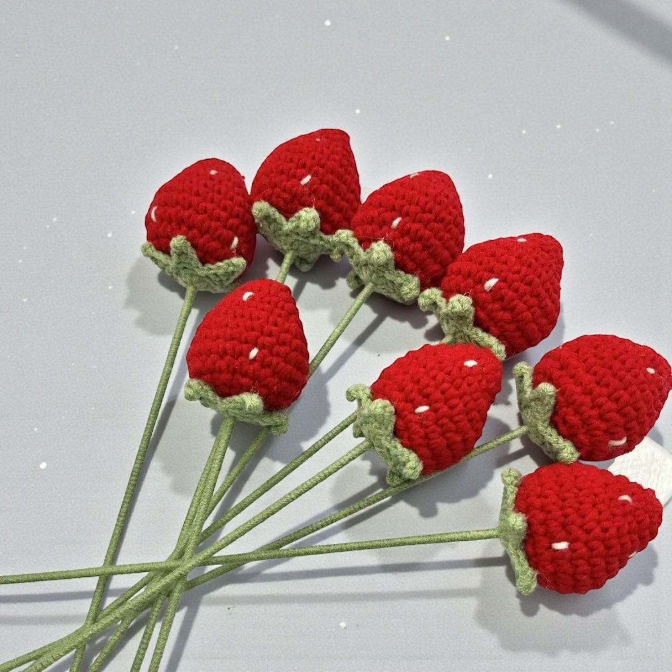 Crocheted red strawberries with green stems on a light gray background