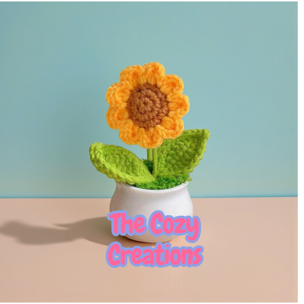 Crocheted sunflower in a pot with 'The Cozy Creations' branding on a light blue and beige background.
