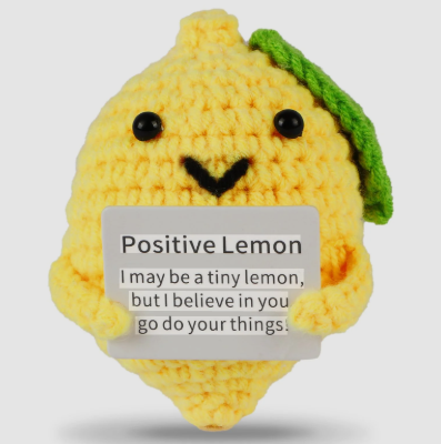 Crocheted lemon character with a message tag on a light gray background