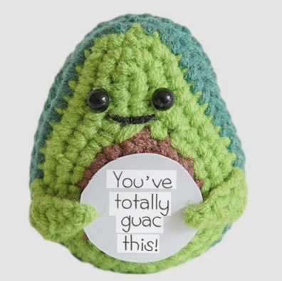 Crocheted avocado plushie with a paper sign saying 'You've totally guac this!' on a white background